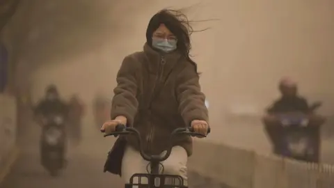 Getty Images A woman cycles along a street during a sandstorm in Beijing on March 15, 2021.