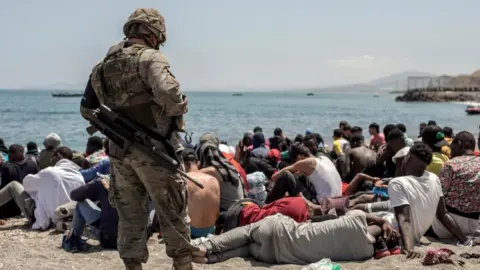 EPA A Spanish soldier looks on at a group of migrants