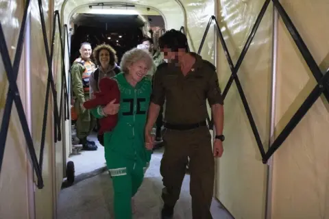 Israel Defense Forces Ruthi Munder holding hands with an IDF soldier, walking down a tunnel after her release