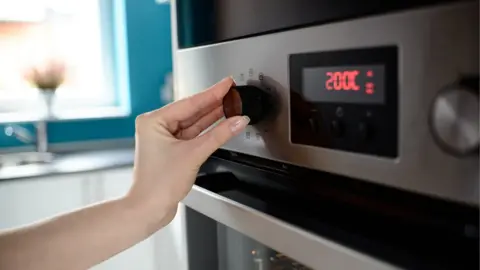 Getty Images Close up of woman's hand setting temperature control on oven.