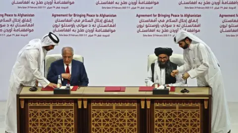 Getty Images US Special Representative Zalmay Khalilzad and Taliban co-founder Mullah Abdul Ghani Baradar sign the peace agreement in February 2020