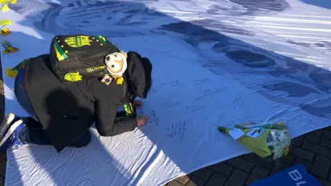 A fan signs a flag tribute to Sala outside the Cardiff City Stadium