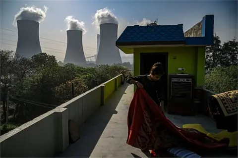 AFP In this photograph taken on April 6, 2022, a girl folds a blanket at her house rooftop near the Thermal Power Corporation (NTPC) plant in Dadri.