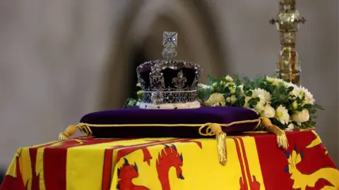 PA Media The coffin of Queen Elizabeth II, draped in the Royal Standard with the Imperial State Crown and the Sovereign's orb and sceptre, lying in state on the catafalque in Westminster Hall