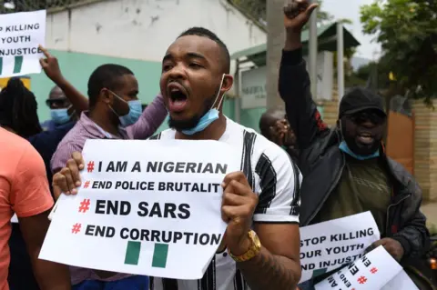 Getty Images A man holds up a sign as people gather to protest outside the Nigerian embassy in Nairobi