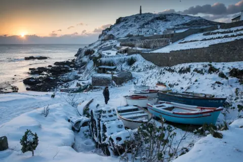 Getty Images The sun sets as snow covers fishing boats left at Priest's Cove at Cape Cornwall near Penzance on 28 February