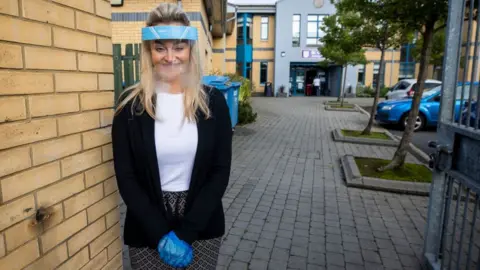 PA Media Ashleigh Clarke, teacher at St Clare's Primary School in Belfast, wearing a protective visor and gloves on Monday 24 August, as P7 pupils are allowed to return to school in Northern Ireland