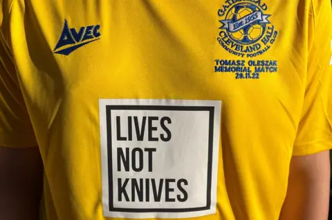 A close up of a yellow football shirt with the lives not knives message