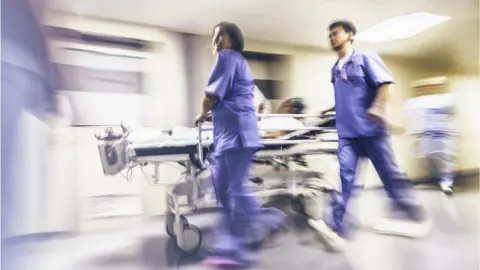 Getty Images A pair of medical staff rush a patient on a trolley through hospital