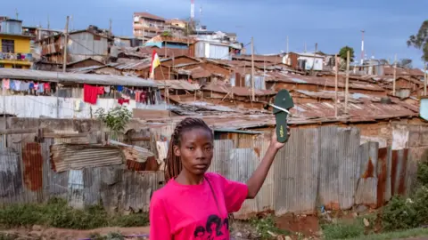 BBC Diana Mwazi standing in front of shacks in Kibera