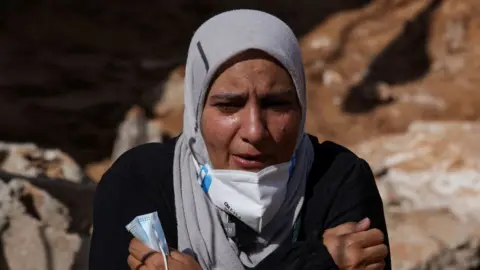 Reuters Sabrine Ferhat Bellil, who said she lost her brother, his wife and 5 of his children when the deadly storm hit her city, reacts as she stands amid rubble beside her brother's destroyed house, where she is hoping to find their bodies to bury, in Derna