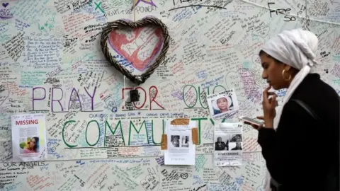 Reuters A woman looks at her smartphone in front of a message board near the scene of the fire that destroyed the Grenfell Tower block