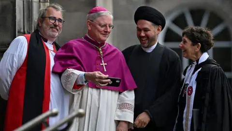 Reuters Faith leaders outside the cathedral, one holding a phone as the others smile