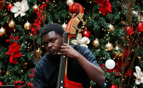 Reuters A man plays the cello in front of a large Christmas tree.