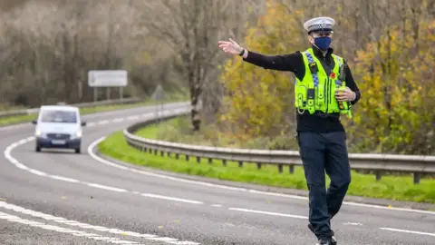 PA Media Lockdown: Dyfed-Powys Police officer pointing to vehicle to stop during checks on essential travel in Carmarthenshire