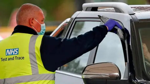 Getty Images NHS employee hands test kit to person in car