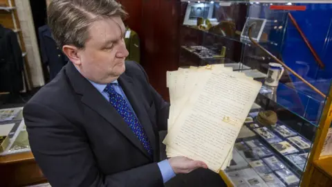 Liam McBurney/PA Media Auctioneer Karl Bennett holding an account of Collins' death written by his close friend Emmet Dalton