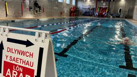 BBC Calon Tysul pool with lane sign in foreground, swimmer's head in pool and lifeguard in background