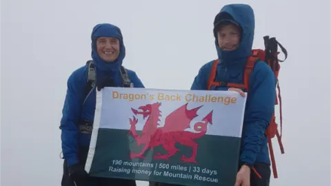 @Dragonchallenge Mike and Matt standing with a flag at the top of Snowdon in the fog