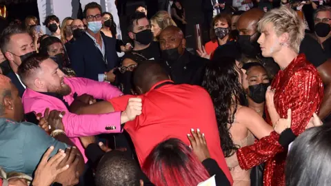 Stephen Lovekin/Shutterstock Conor McGregor being held back and Machine Gun Kelly on the red carpet