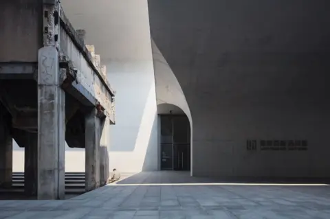 Pawel Paniczko / APA18 A man sitting on the ground surrounded by concrete architecture