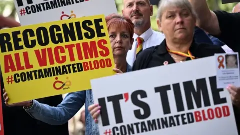 Getty Images Protestors hold placards with message related to the NHS infected blood scandal as Prime Minister Rishi Sunak gives evidence to the Infected Blood Inquiry in London, on 26 July, 2023