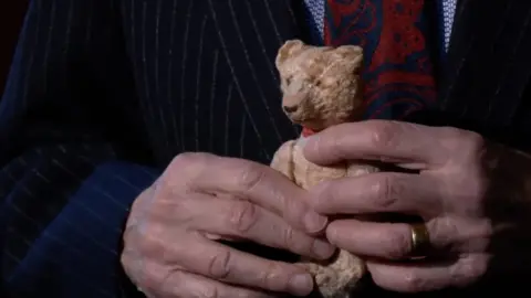 A Holocaust survivor holds up the childhood teddy that helped him brave the Nazis.