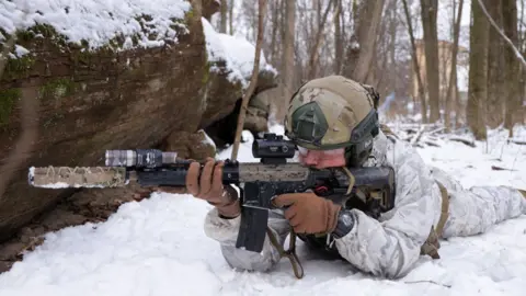 Getty Images A civilian participant in a Kyiv Territorial Defence unit waits to fend off a mock attack while training on a Saturday in a forest on January 22, 2022 in Kyiv