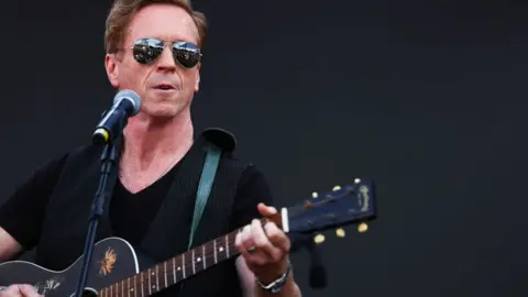 Getty Images Damian Lewis performing with a guitar