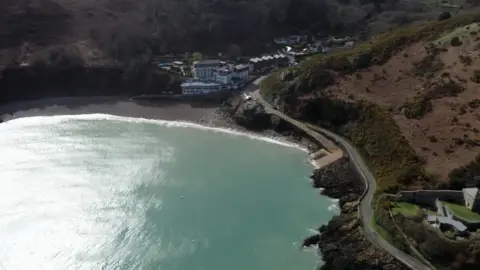 BBC a high up shot of bouley bay - the sea beside a road and lots of woodland