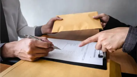 Getty Images / Ngampol Thongsai / EyeEm passing envelope in a deal