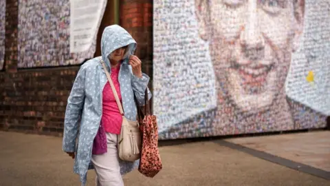 Getty Images Woman walking in rain in front of street art.