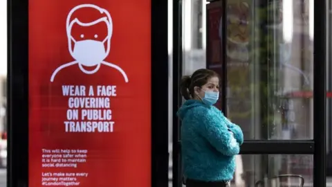Getty Images Woman at bus stop wearing a face mask
