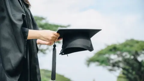 Boy_Anupong a person in a black graduation gown holding a cap