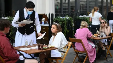 Getty Images Man in mask serves diners outdoors