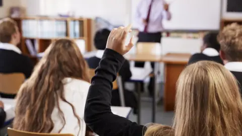 Getty Images Girl putting her hand up to ask a question in school