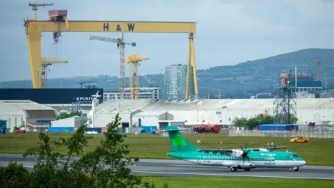 Jonathon Graham @AVGeek_NI An Aer Lingus plane landing at Belfast City Airport with a Harland and Wolff shipyard crane in the background