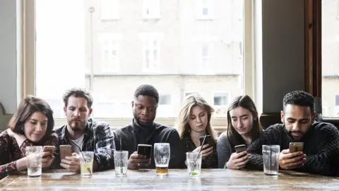 Getty Images A group of people in a pub all looking at their phones (stock photograph)