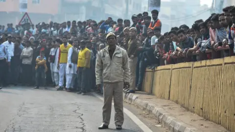 AFP A policeman and onlookers gather near a factory fire in Delhi