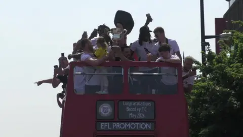 BBC Bromley players raise a football cup as they travel through the town on a bus