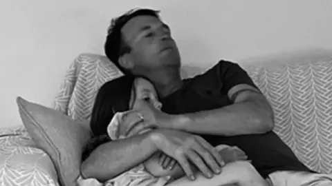 Hollie McFarlane Hollie's husband Mike cuddling Sydney on the sofa. The photo has a black and white treatment.