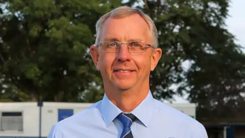 Richard Chappell Photography Neil Blackmore looks into the camera, wearing glasses and a blue shirt & tie