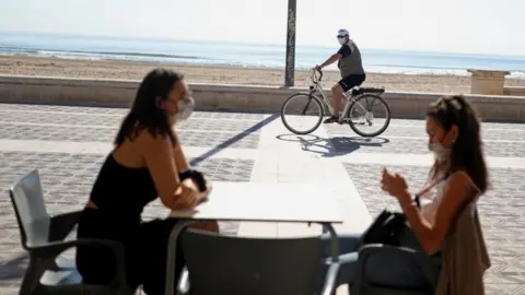 Reuters Women wearing protective masks sit on a terrace of a restaurant at Malvarrosa beach, as some Spanish provinces are allowed to ease lockdown restrictions during phase one, amid the coronavirus disease (COVID-19) outbreak, in Valencia, Spain May 18,