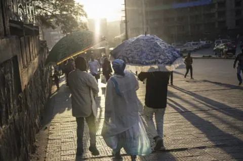MICHELE SPATARI/AFP Ethiopian Orthodox Christians walk down the street, wearing white clothes and carrying embroidered umbrellas.
