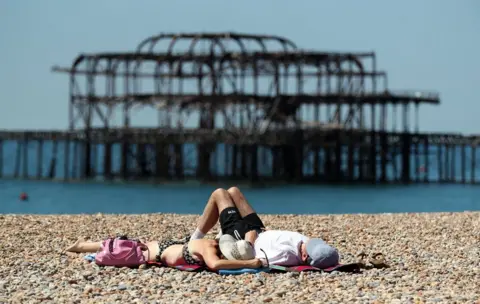 PA People relax in the sunshine on the beach in Brighton, Sussex