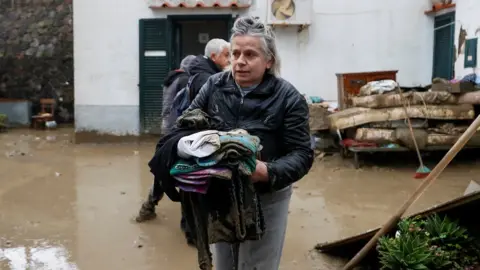 Ciro de Luca/Reuters A resident carries some belongings covered in mud