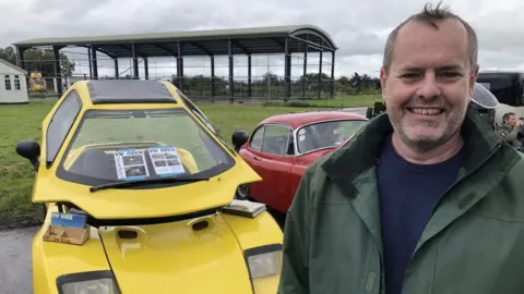 BBC Rob Barton standing next to a yellow Volkswagen Nova