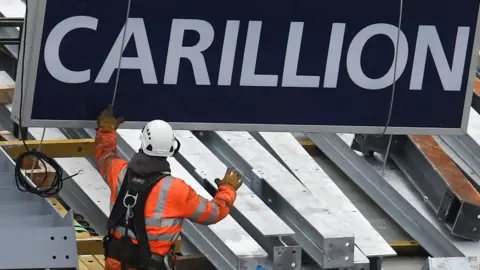 AFP A construction worker guides down a sign showing the name of Carillion