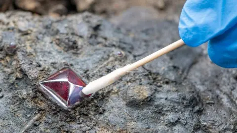 MOLA/Andy Chopping Archaeologist examining a garnet