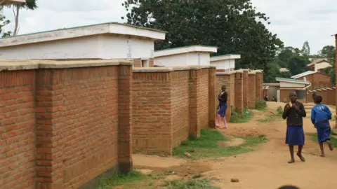 WaterAid A row of red-brick toilet blocks stretches down the earthen path in Mloza school, as students make their way to and from class